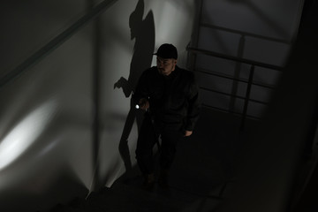 Fototapeta na wymiar Male security guard with flashlight going up stairs in darkness