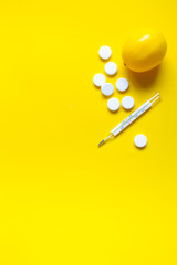 Lemon, thermometer and white medical pills on yellow background, pharmacy theme, treatment and prevention of virus. Concept of health in season of colds.