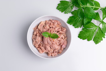 Canned tuna in a white bowl, isolated on white; empty open tuna tin on a white background; copy space, soft light, studio shot