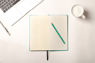 Work space with laptop, turquoise notebook and cappuccino on white table. Flat lay