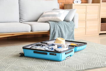 Open suitcase with packed clothes and accessories on floor at home