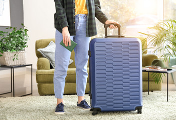 Young woman with packed suitcase and passport at home
