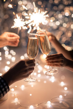 Hands of friends holding flutes of champagne and sparkling Bengal lights