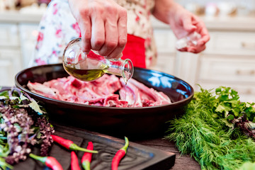 Cook adds oil to raw lamb ribs on frying pan close up