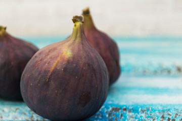 Three fresh figs on a wooden white table. Arranged in a row.