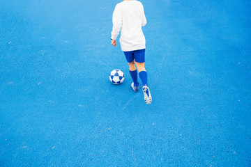 Little unrecognizable boy playing soccer of blue background
