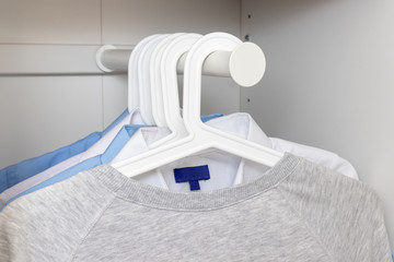 Fototapeta na wymiar Pastel color clothes casual cotton sweatshirts and classic shirts hanging on white plastic hangers on a rack in wardrobe