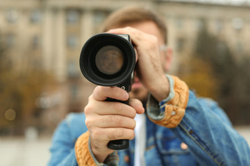 Young man with vintage video camera on city street, focus on lens