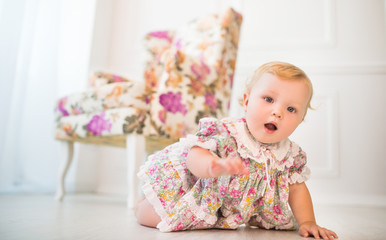 Charming girl in floral dress crawls on floor