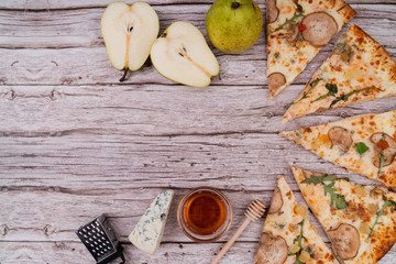 pizza pieces on wooden background decorated with pear, blue cheese and honey