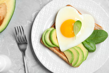 Tasty breakfast with heart shaped fried egg served on  grey table, flat lay