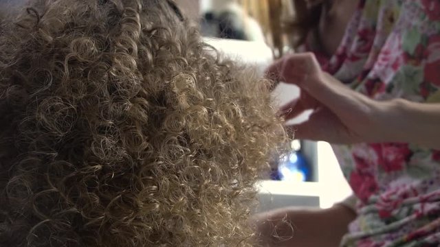 Stylist makes curly afro hairstyle for woman by hot curling hair, process of making hairstyle, hairstyles in the beauty salon