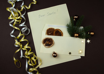 Dear santa letter written for Christmas. Paper and envelope with branch of spruce and dried slice of orange on brown surface.