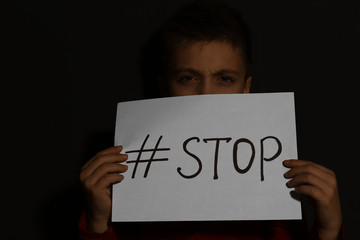 Abused little boy with hashtag STOP near black wall. Domestic violence concept