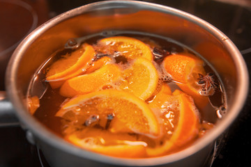 Making hot alcoholic mulled wine with oranges and spices. Christmas beverages boil in the metal pan. Glintwine from rose wine with citrus, cloves, star anise, cinnamon.