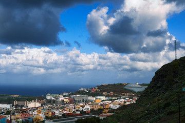 D&iacute;a lluvioso con cielo nublado y donde se ve unos riscos en primer plano y parte de ciudad en segundo plano.