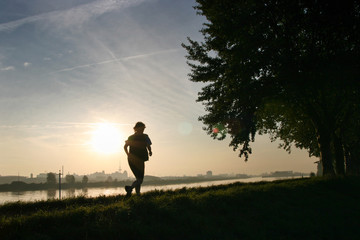 Silhouette of a Woman jogging outdoors with the city of Bremen and sunrise in the background