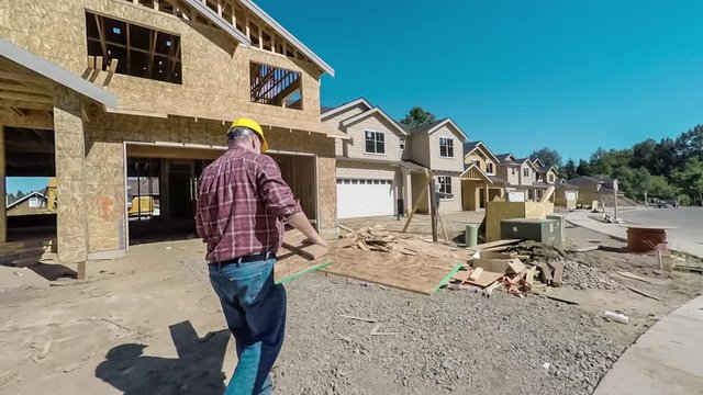 Mature male construction worker experiences severe back pain while carrying lumber, cleaning up a job site