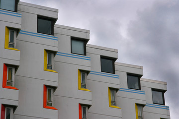 Detail of a facade of a residential building with red, yellow and blue details with moody sky in the background