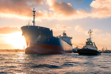 Amazing cloudy sunrise during mooring operations in port. The huge tanker is receiving tugboat...