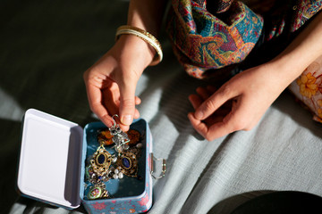 Woman at home examines a beautiful decoration in a jewelry box, hands close-up