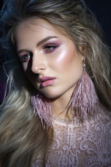 Low light photo of a very beautiful girl with professional tender pink makeup, green eyes and ostrich feather earrings.
