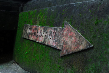A sing indicating the path to the beach. Wall covered with moss. Arrow.