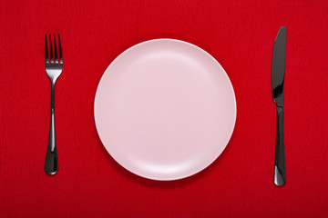 White empty plate with fork and knife on a red tablecloth