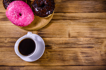 Cutting board with glazed donuts and cup of coffee on a wooden table. Top view