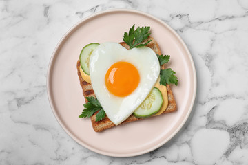 Plate of tasty sandwich with heart shaped fried egg on white marble table, top view