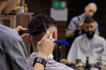 Hair styling and cutting with razor. Close-up rear view of young bearded man getting haircut by hairdresser at barbershop. Advertising and barber shop concept.