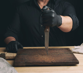 chef in a black shirt and black latex gloves holds a large kitchen knife