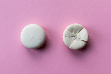 Broken macaroon cake compared to other unbroken on the pink background. The concept of non-ideality, identity; loss and broken soul