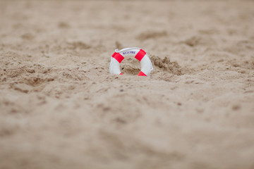 Close-up Of Miniature Lifebuoy Dig In The Sand At Beach