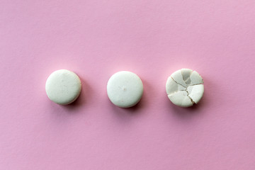Broken macaroon cake compared to other unbroken on the pink background. The concept of non-ideality, identity; loss and broken soul