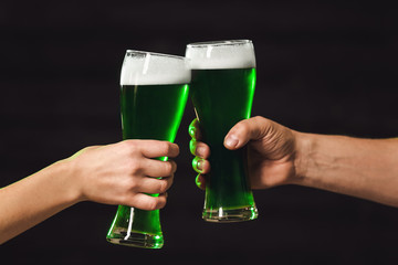 People drinking green beer on St. Patrick's Day against dark background