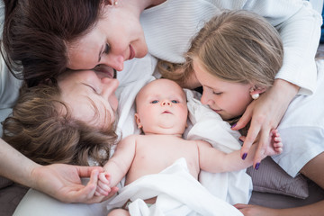 Top view happy positive Young family husband wife and little newborn baby lie on a cozy bed....