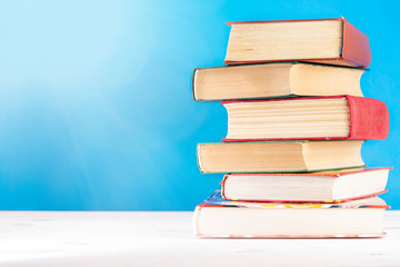 Stack of old books, blue background, free copy space. Antique old hardback books on a wooden shelf on a deck table, unmarked, empty spine. Back to school. Education