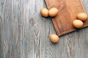 Board with fresh eggs on wooden background