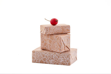 There are three small beige gift boxes on a white background and a red berry. The concept of celebration, joy, surprises.