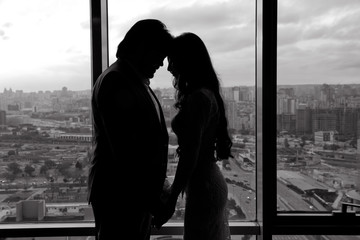 The bride and groom in a cozy house, photo taken with natural light from the window. Silhouette of bride beautiful young woman and groom handsome man share love head to head on background of window .