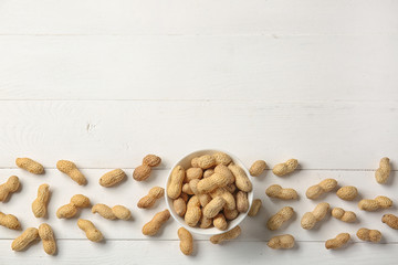 Bowl with peanuts on white wooden background