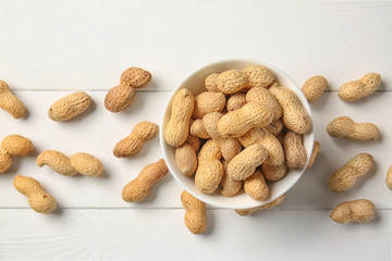 Bowl with peanuts on white wooden background