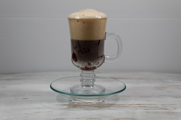 On a table on a transparent saucer is a mug of beer with a cap of foam on top and bubbles below.