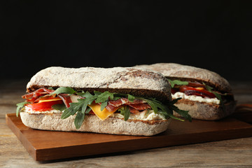 Delicious sandwich with fresh vegetables and prosciutto on wooden table
