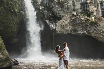 Spanish couple in love kissing with amazing view of waterfall. Happy together, honeymoon in Bali. Travel lifestyle. Wanderlust concept. 