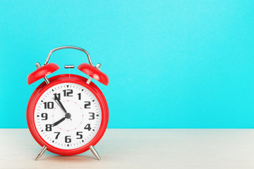 Red retro alarm clock with five minutes to eight o'clock, on wooden table on a blue background. The concept of time, holiday, 5 minutes to the event, deadline. Layout with copy space for your text.