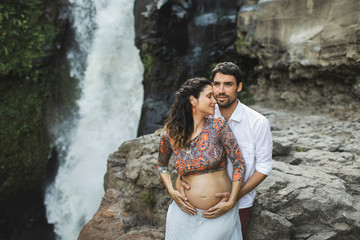 Portrait of young pregnant latin american couple in love outdoors. Family values. Happy together and smiling, pregnancy travel lifestyle. Naked belly.