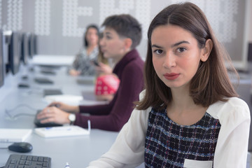 Side view of students using computer in lab. IT student looking and smiling into camera during class inside computer lab.