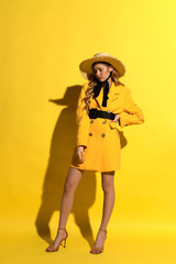 Pretty blonde girl with freckles in yellow outfit and straw hat on yellow background